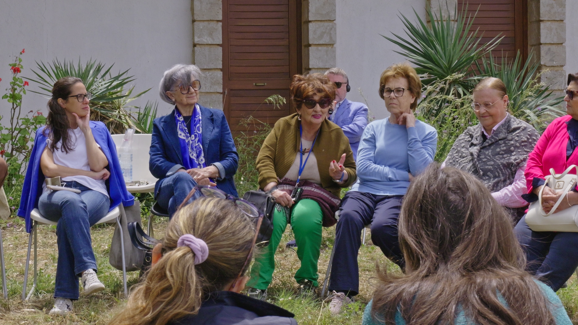 Una donna parla a un gruppo di persone sedute in un cerchio all'aperto.