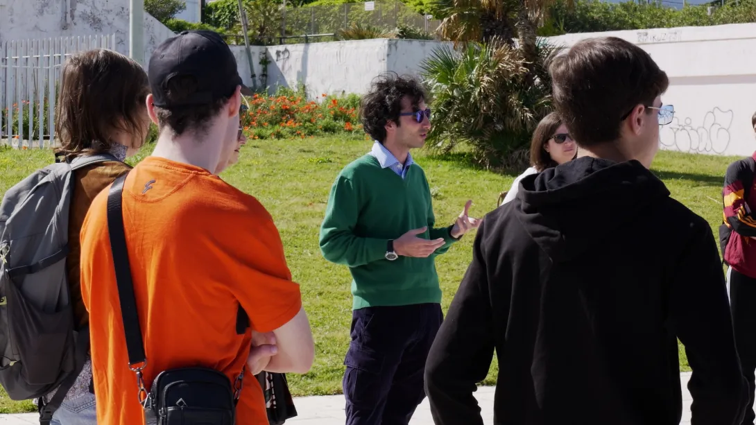 Un uomo parla a un gruppo di persone, all'aperto.